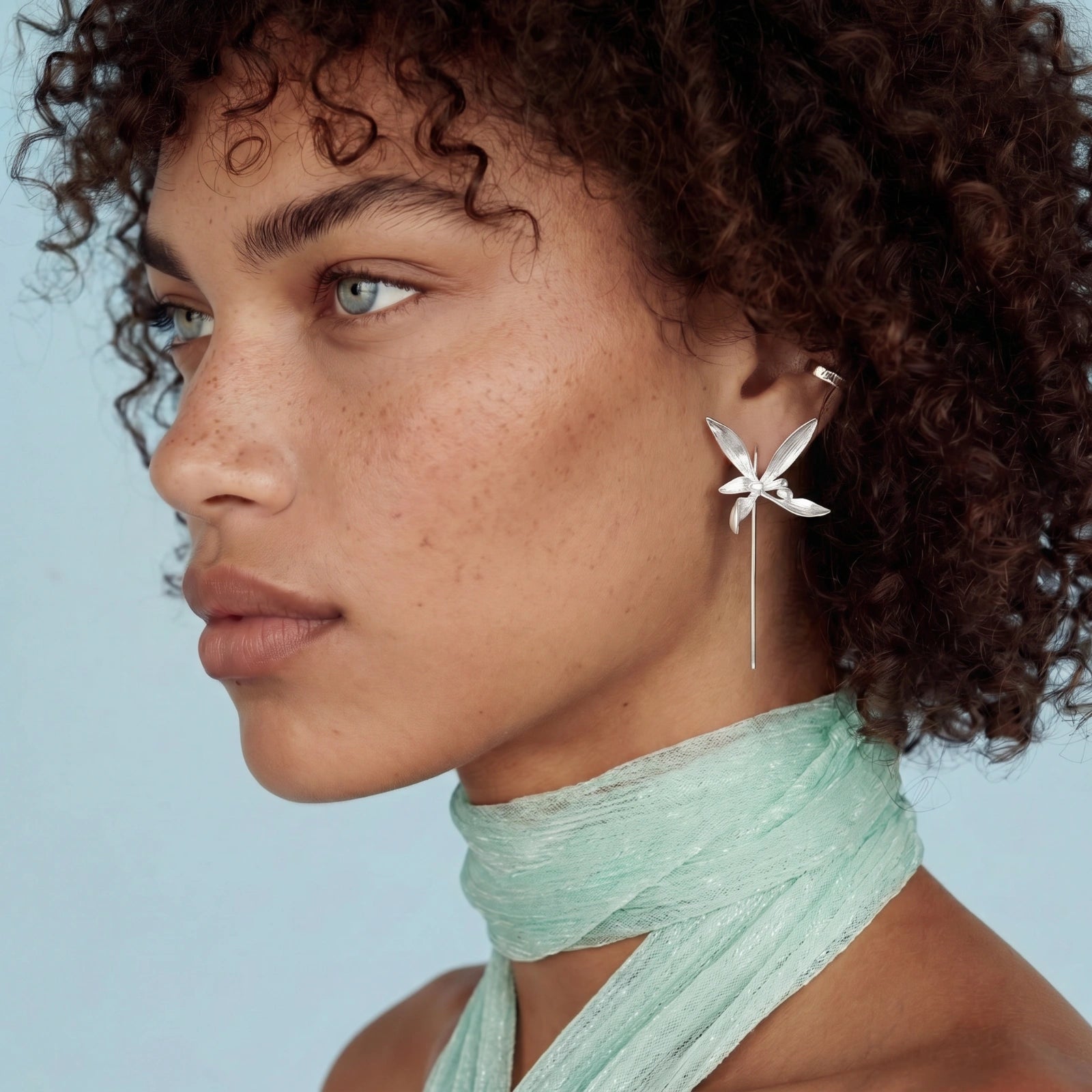 Close-up of a woman wearing a floral earring with a light blue background
