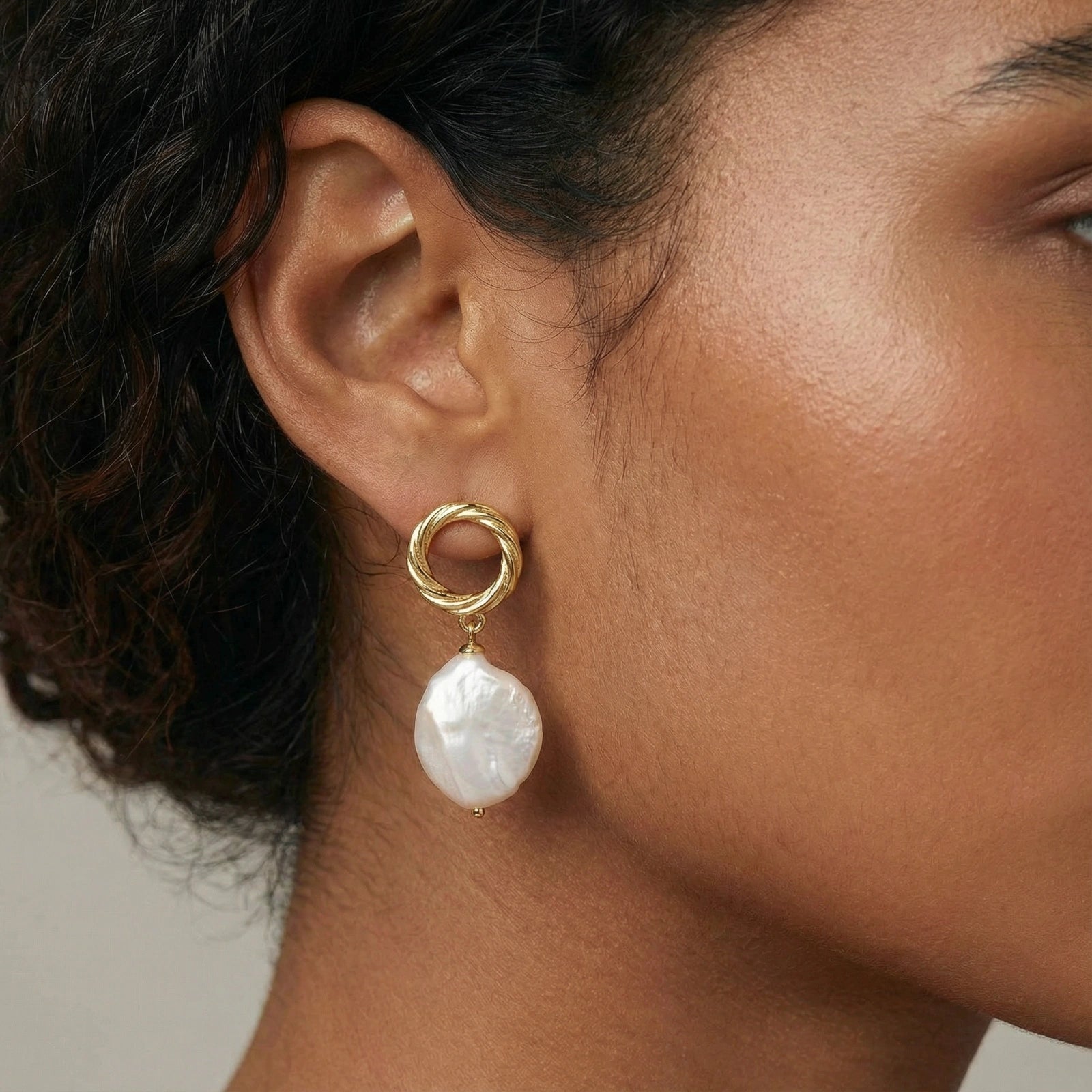 Close-up of a person wearing a gold earring with a pearl drop.