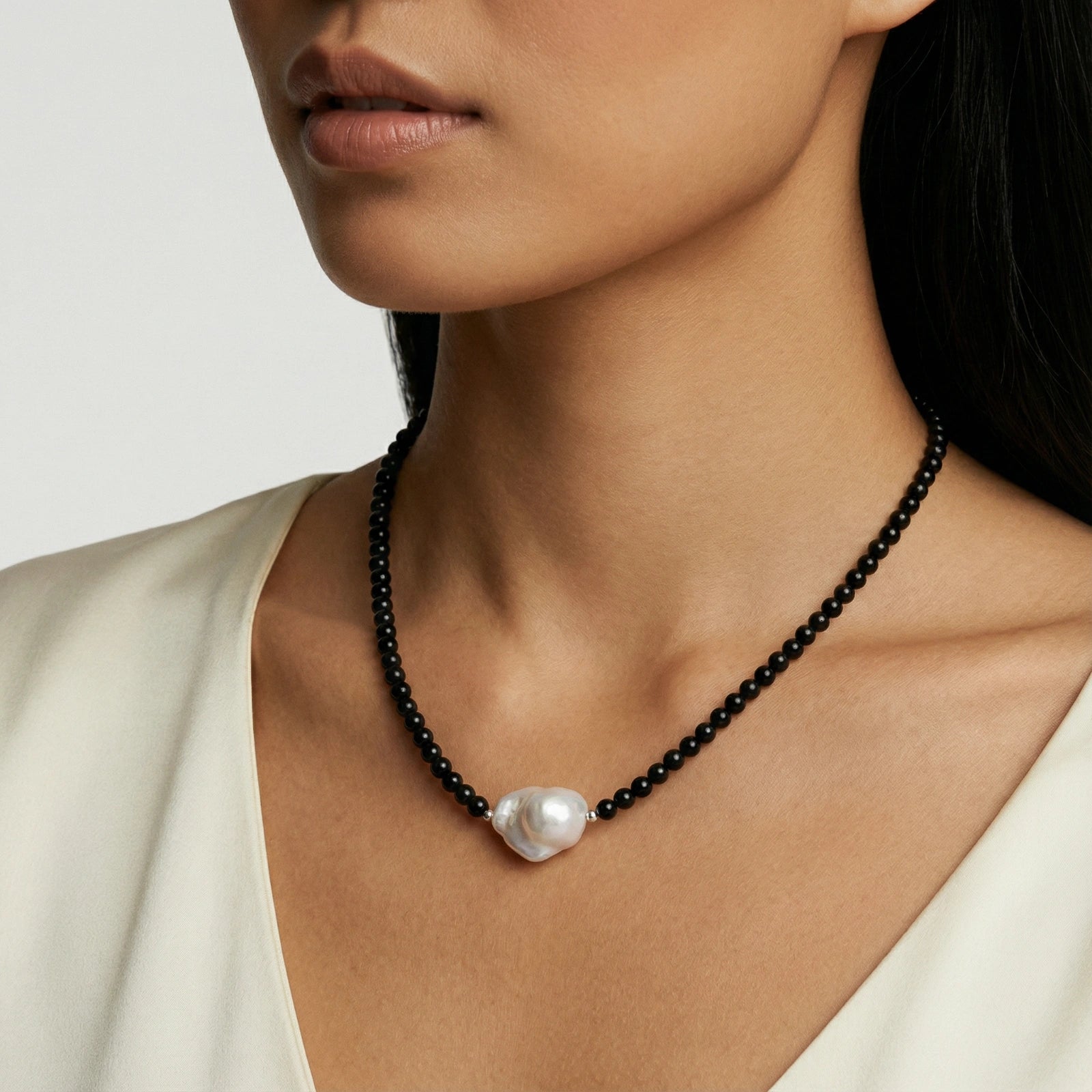 Black beaded necklace with a large white pearl pendant on a model against a neutral background
