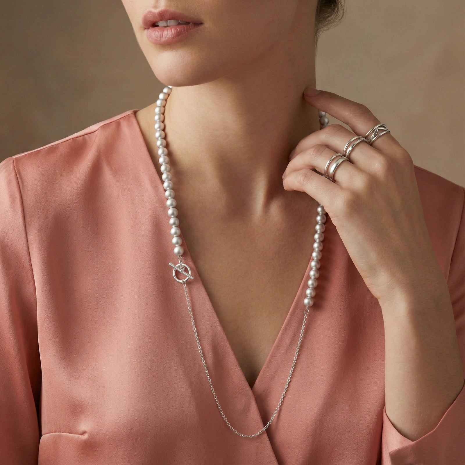Woman wearing a pearl necklace and rings on a neutral background