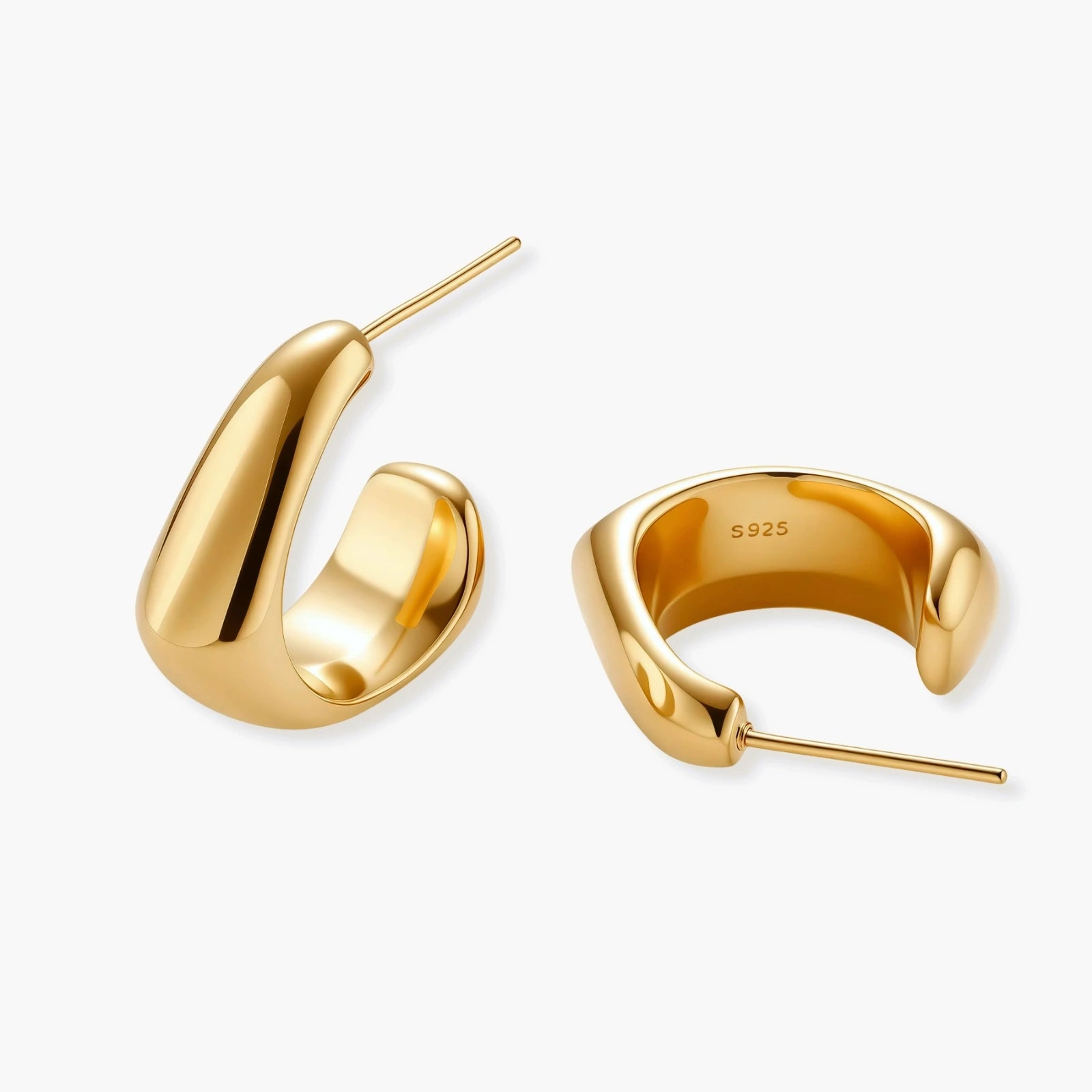 Close-up of curved gold-plated huggie earrings with sculptural design on white background, showing polished finish.