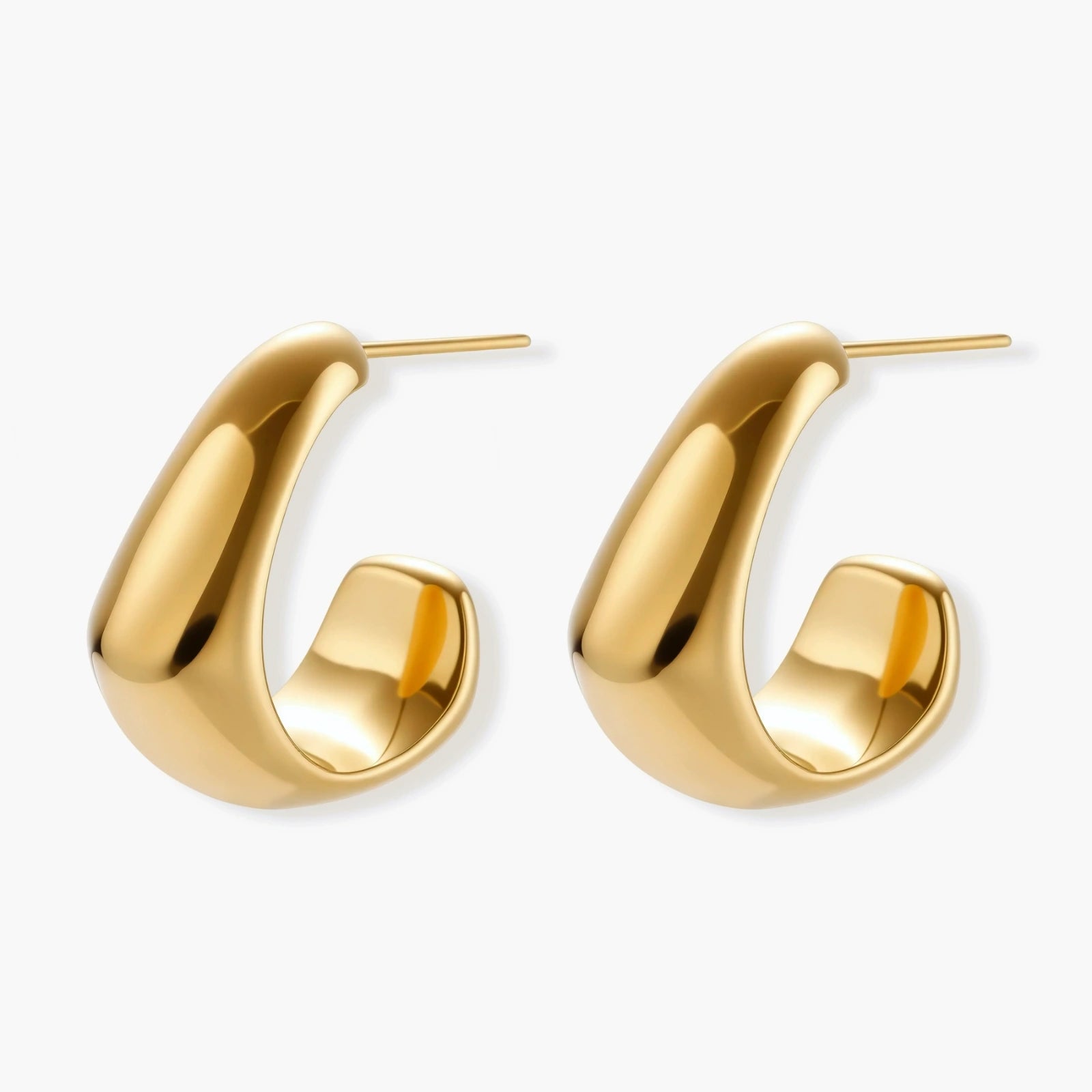 Close-up of curved gold-plated huggie earrings with sculptural design on white background, showing polished finish.
